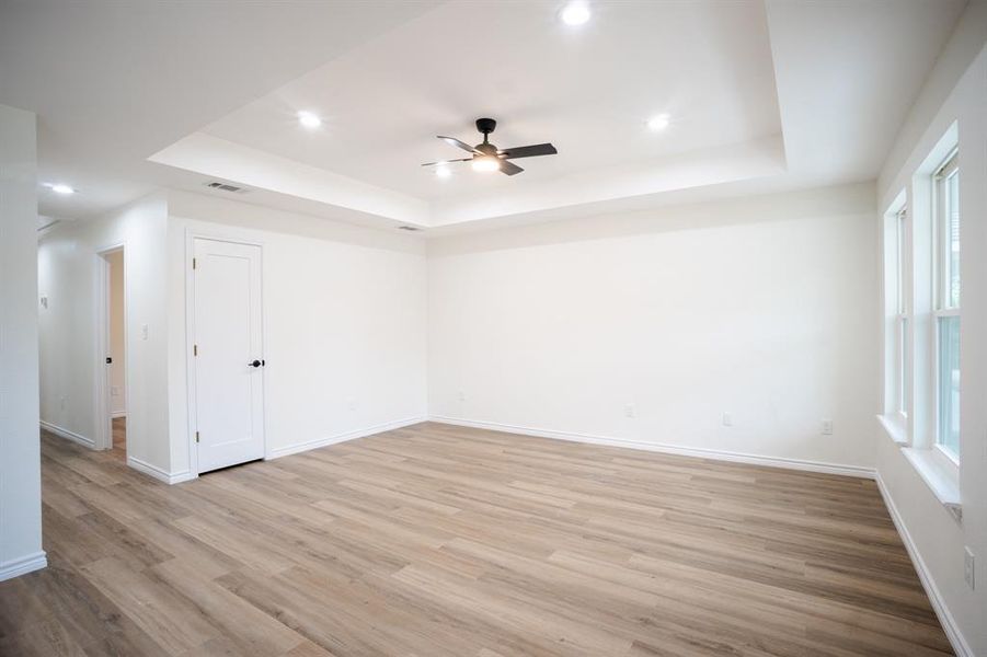 Spacious room featuring wood-finish flooring, a tray ceiling with recessed lighting, and a ceiling fan