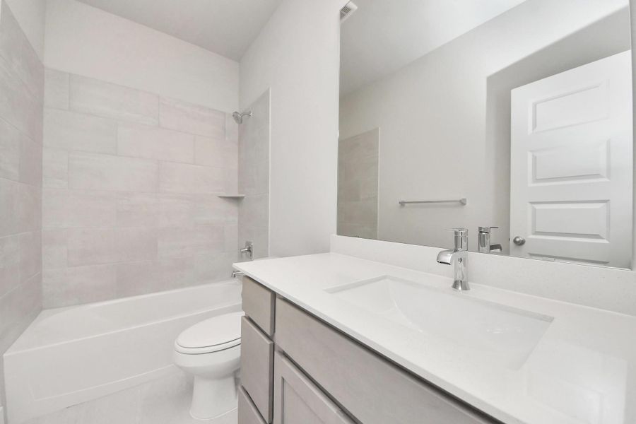 Secondary bath features tile flooring, bath/shower combo with tile surround, light stained wood cabinets, beautiful light countertop. Sample photo of completed home with similar floor plan. Actual colors and selections may vary.