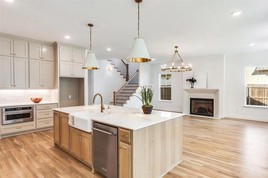 Kitchen with a fireplace, light wood-type flooring, hanging light fixtures, light stone counters, and recessed lighting