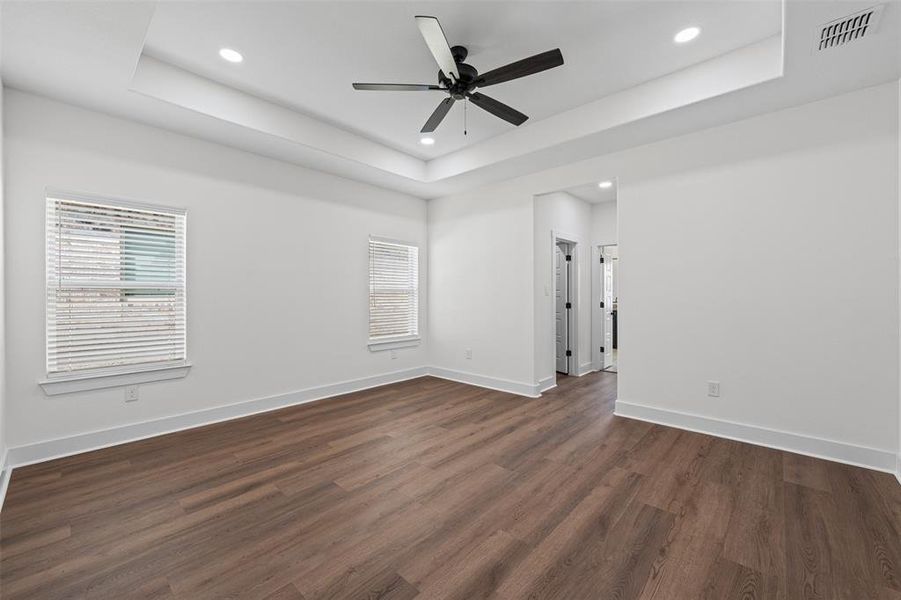 Spacious room featuring wood-look flooring, white walls, and a tray ceiling with recessed lighting and a ceiling fan