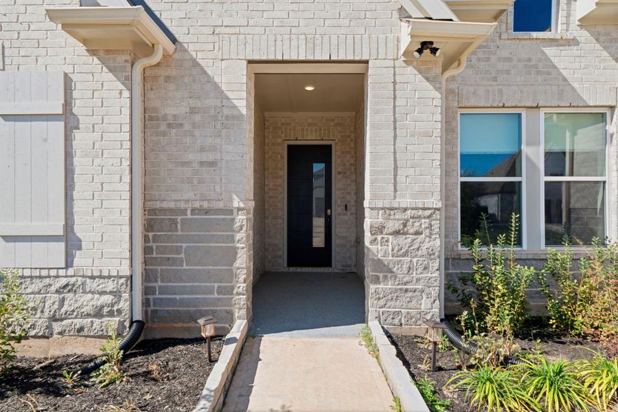 Inviting covered entry with modern front door, upgraded brick and stone accents, and clean, well-maintained landscaping.