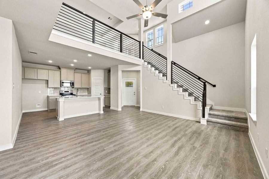 Open-concept living area with two-story ceiling, staircase, and kitchen with island Open-concept living area with two-story ceiling, staircase, and kitchen with island