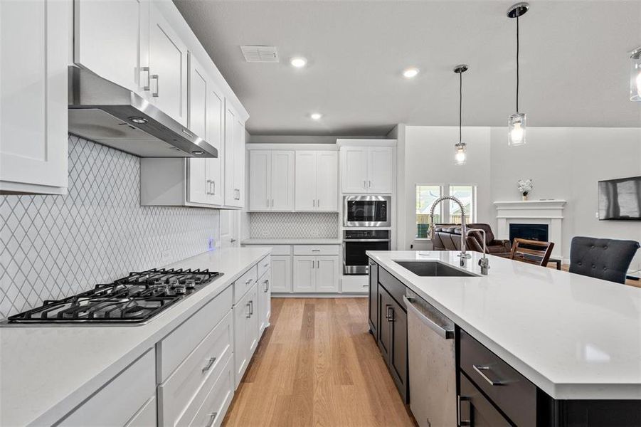 Kitchen with sink, light wood-type flooring, an island with sink, white cabinetry, and stainless steel appliances