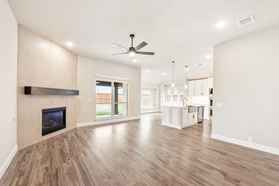 Open-concept living room with fireplace and wood floors, open to kitchen with white island and pendant lights Open-concept living room with fireplace and wood floors, open to kitchen with white island and pendant lights