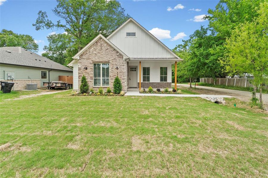 Contemporary Craftsman-style home featuring a brick and vertical siding facade, a covered front porch with wood columns, a prominent gable roofline, and a manicured front lawn