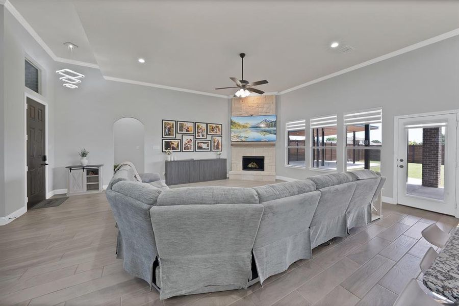Living area with arched walkways, a ceiling fan, crown molding, a large fireplace, and baseboards Living area with arched walkways, a ceiling fan, crown molding, a large fireplace, and baseboards