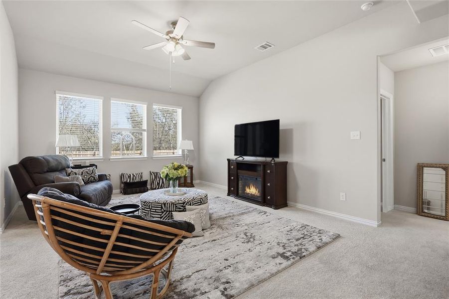 Living area featuring a vaulted ceiling with ceiling fan, three large windows, and neutral carpeting