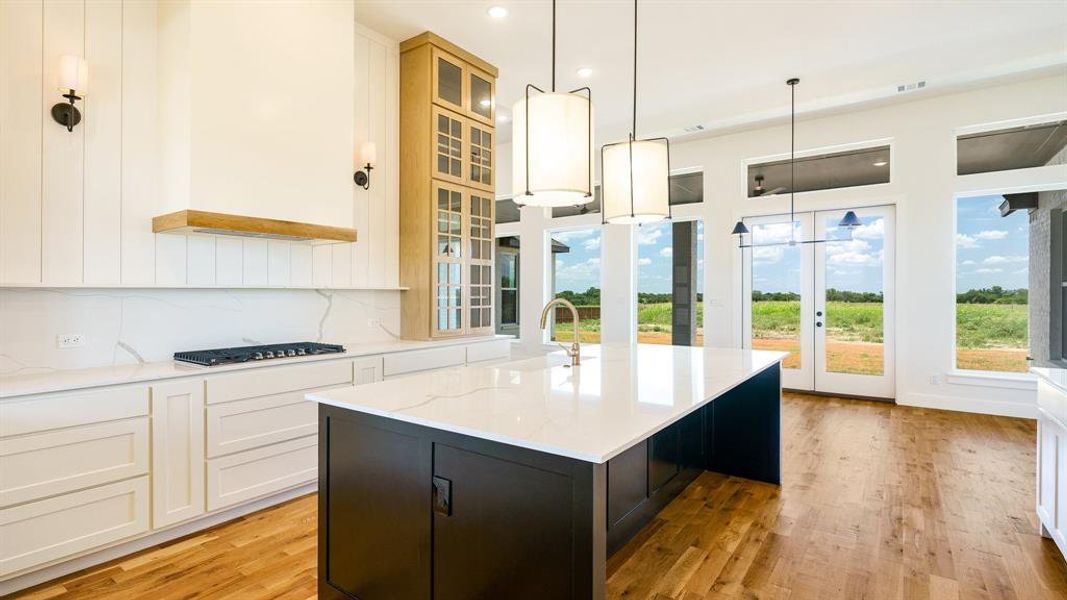 Kitchen featuring an island with sink, gas stovetop, sink, light hardwood / wood-style floors, and decorative light fixtures