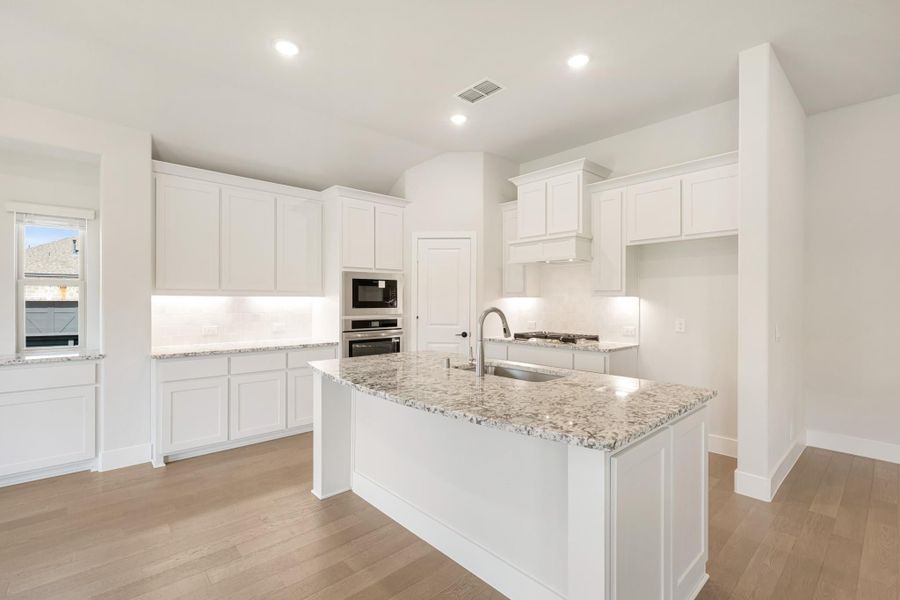 White kitchen with granite island, stainless steel appliances, and light hardwood floors