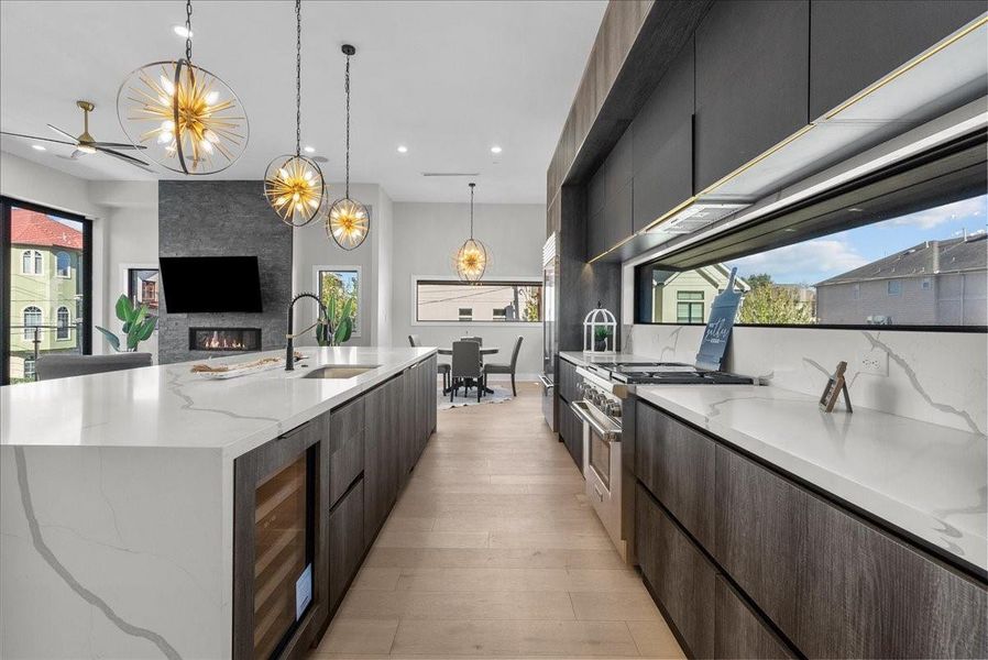 This modern kitchen features sleek dark cabinetry, marble countertops, and elegant pendant lighting. It includes a spacious island with a sink, a built-in wine cooler, and large windows providing abundant natural light. The open layout flows into a dining area, complemented by a cozy fireplace and contemporary decor. This modern kitchen features sleek dark cabinetry, marble countertops, and elegant pendant lighting. It includes a spacious island with a sink, a built-in wine cooler, and large windows providing abundant natural light. The open layout flows into a dining area, complemented by a cozy fireplace and contemporary decor.