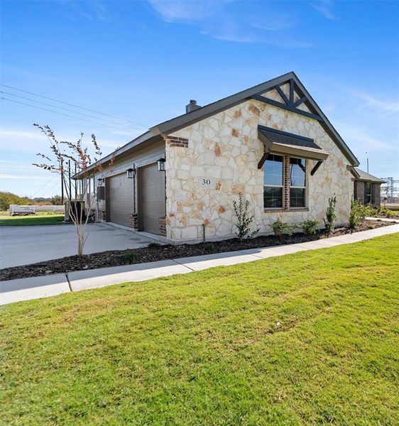 View of front of house featuring stone siding, concrete driveway, a garage, and a front yard