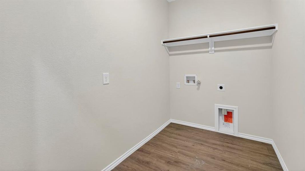 Dedicated laundry area featuring wood-finish flooring, light neutral wall tones, and a built-in shelf with hanging rod Dedicated laundry area featuring wood-finish flooring, light neutral wall tones, and a built-in shelf with hanging rod