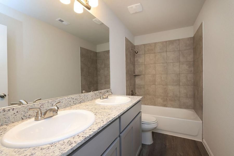 The en-suite bathroom features a sleek double vanity with granite countertops, a large mirror, and a bathtub with tiled walls. Just add bubbles!