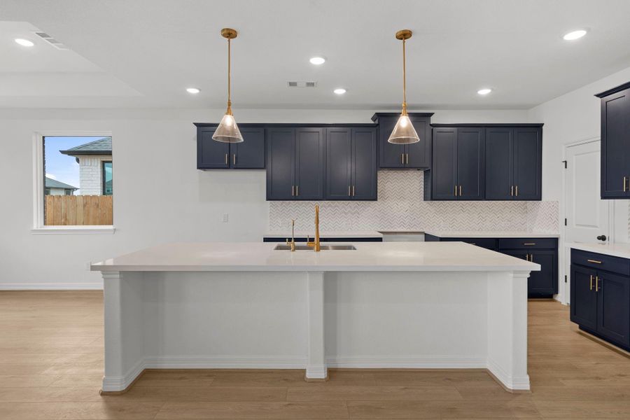 This light and bright kitchen features a large quartz island, custom stained cabinets, a large sink overlooking your family room, recessed lighting, and beautiful backsplash.