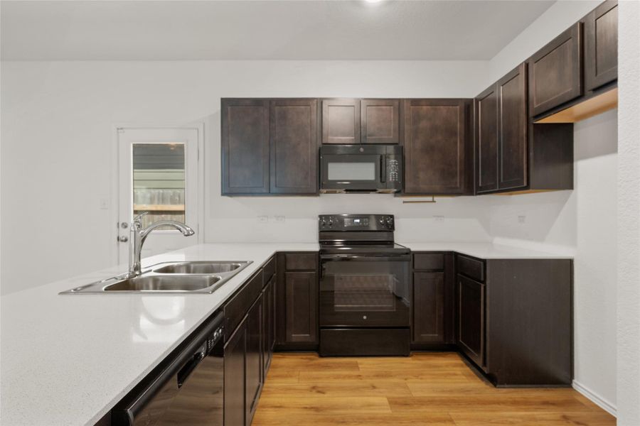 Kitchen featuring black appliances, light countertops, dark brown cabinetry, and light wood-type flooring Kitchen featuring black appliances, light countertops, dark brown cabinetry, and light wood-type flooring