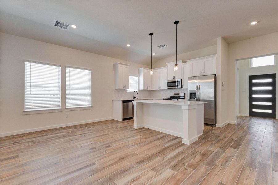 The heart of the home shines in this open-concept kitchen and living area, where functionality meets modern style. The oversized island with quartz countertops provides ample prep space and seating, while pendant lighting adds a designer touch. Flowing seamlessly into the main living area, this space is ideal for entertaining or everyday living, enhanced by durable wood-look tile flooring.