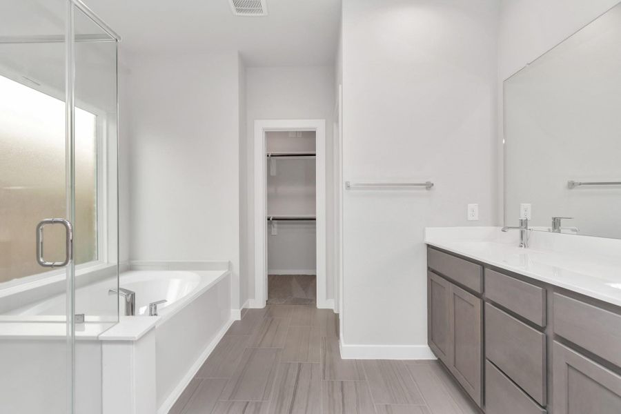 Enjoy a walk-in shower with tile surround, a separate garden tub with custom detailing, and an elegant vanity featuring light countertops, and modern hardware. Experience luxury and relaxation in every detail. Sample photo of completed home with similar floor plan. As-built interior colors and selections may vary. Enjoy a walk-in shower with tile surround, a separate garden tub with custom detailing, and an elegant vanity featuring light countertops, and modern hardware. Experience luxury and relaxation in every detail. Sample photo of completed home with similar floor plan. As-built interior colors and selections may vary.
