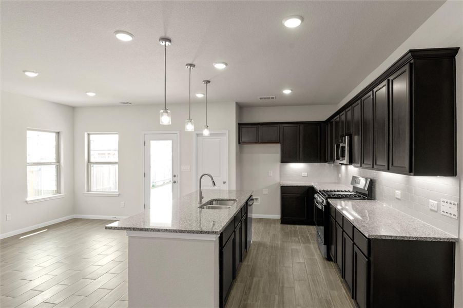 Kitchen featuring stainless steel appliances, backsplash, wood finish floors, light stone counters, and recessed lighting