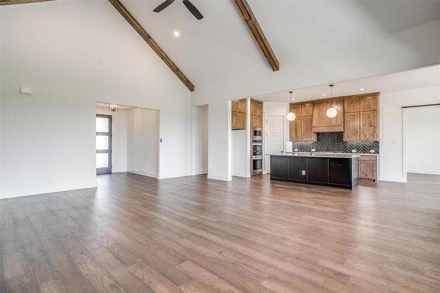 Unfurnished living room with high vaulted ceiling, dark hardwood / wood-style floors, ceiling fan, and beam ceiling