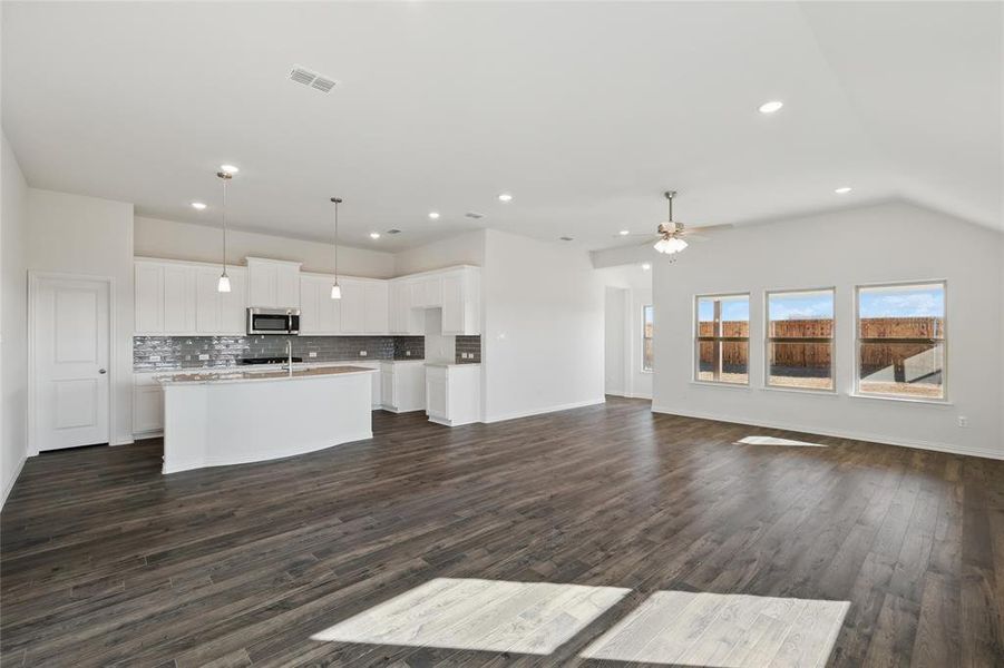 Kitchen featuring open floor plan, a kitchen island with sink, white cabinetry, backsplash, and hanging light fixtures