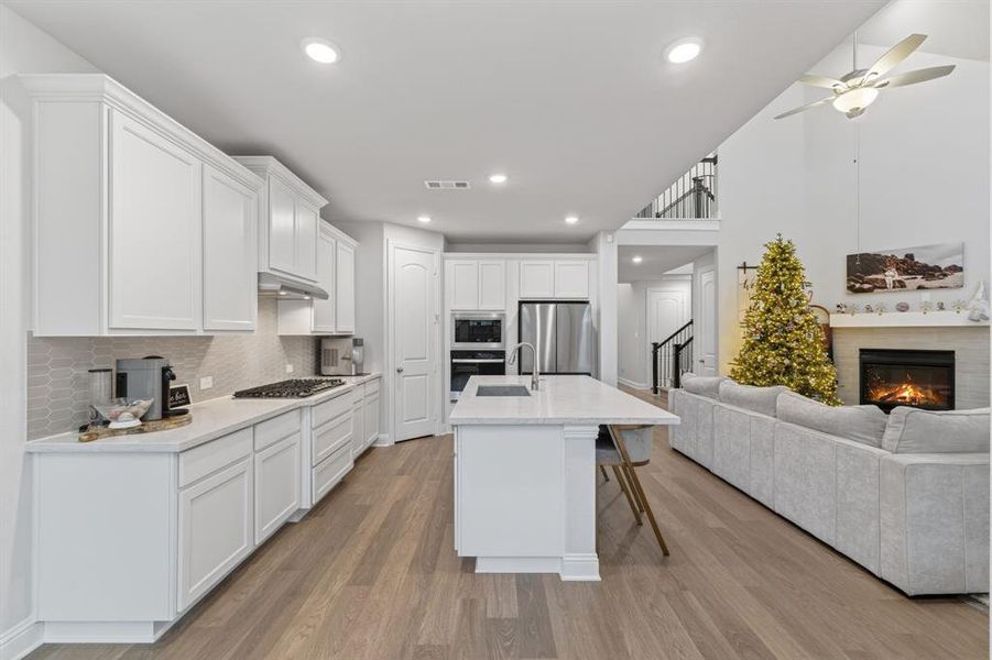 Kitchen with a breakfast bar area, open floor plan, white cabinetry, light wood-type flooring, and stainless steel appliances Kitchen with a breakfast bar area, open floor plan, white cabinetry, light wood-type flooring, and stainless steel appliances