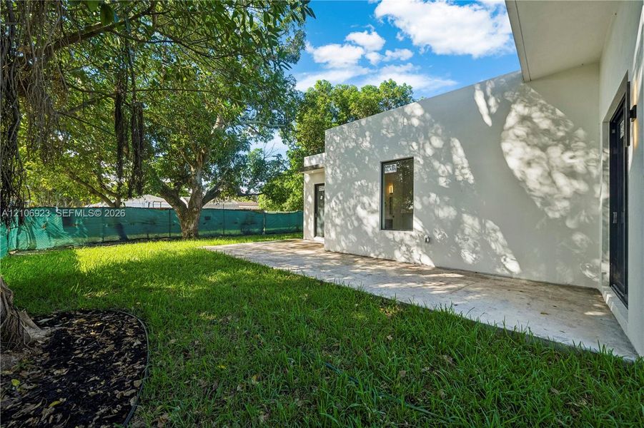 Backyard featuring a paved patio, manicured lawn, mature trees, and an exterior light fixture Backyard featuring a paved patio, manicured lawn, mature trees, and an exterior light fixture