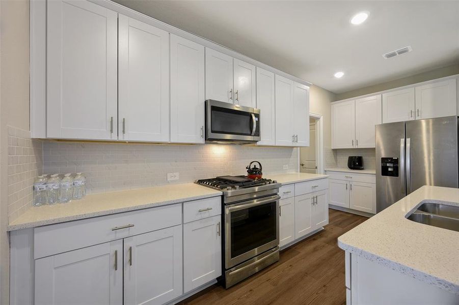 Modern kitchen featuring white shaker-style cabinetry, light-toned countertops, a full suite of stainless steel appliances, and wood-finish flooring Modern kitchen featuring white shaker-style cabinetry, light-toned countertops, a full suite of stainless steel appliances, and wood-finish flooring
