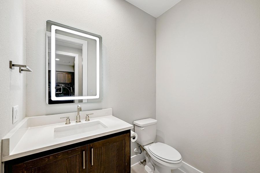 A well-appointed half-bath with a stylish vanity and a sleek, illuminated mirror.