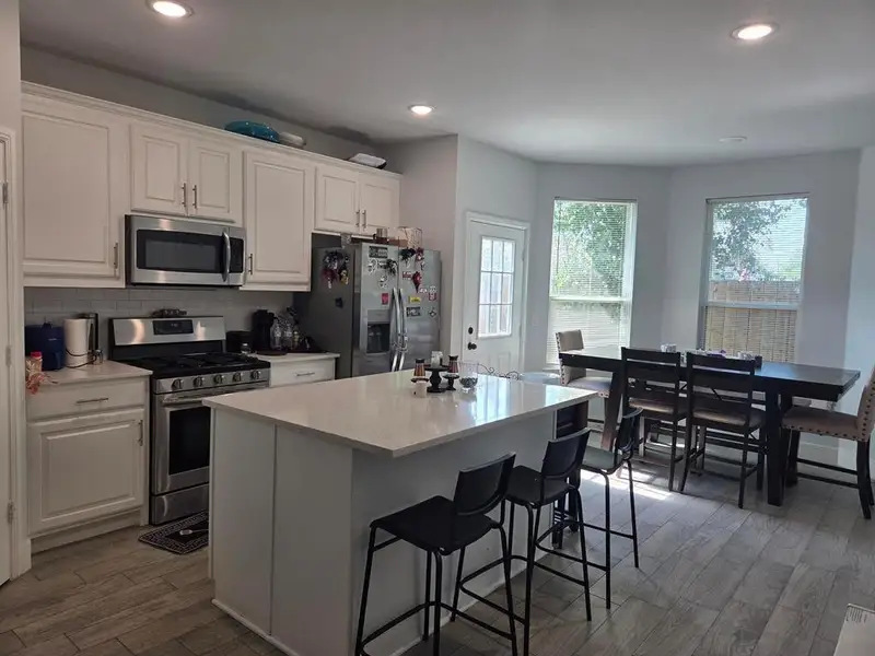 Kitchen with stainless steel appliances, white cabinets, light wood-style flooring, a breakfast bar, and tasteful backsplash