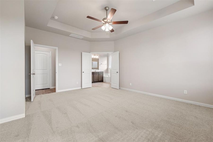 Unfurnished bedroom featuring a raised ceiling, light carpet, a ceiling fan, and connected bathroom Unfurnished bedroom featuring a raised ceiling, light carpet, a ceiling fan, and connected bathroom