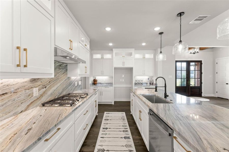 Kitchen featuring glass insert cabinets, decorative backsplash, white cabinets, decorative light fixtures, and light stone countertops Kitchen featuring glass insert cabinets, decorative backsplash, white cabinets, decorative light fixtures, and light stone countertops