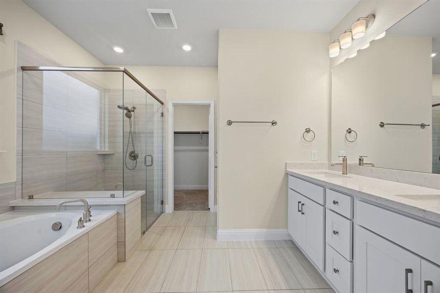 Full bathroom featuring a spacious closet, double vanity, a stall shower, a bath, and light tile patterned flooring