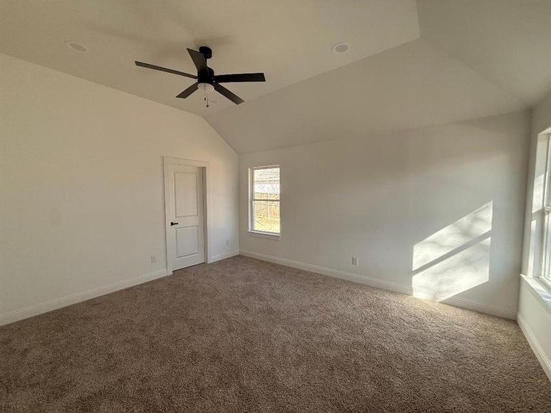 Carpeted spare room featuring vaulted ceiling and a ceiling fan