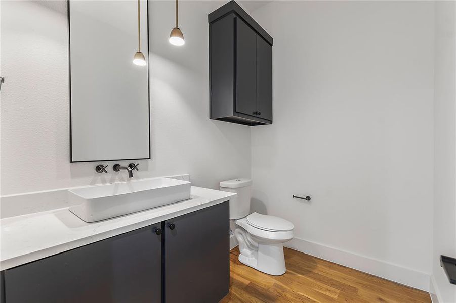 Modern bathroom featuring wood-finish flooring, a rectangular vessel sink, a wall-mounted faucet, and dark cabinetry Modern bathroom featuring wood-finish flooring, a rectangular vessel sink, a wall-mounted faucet, and dark cabinetry