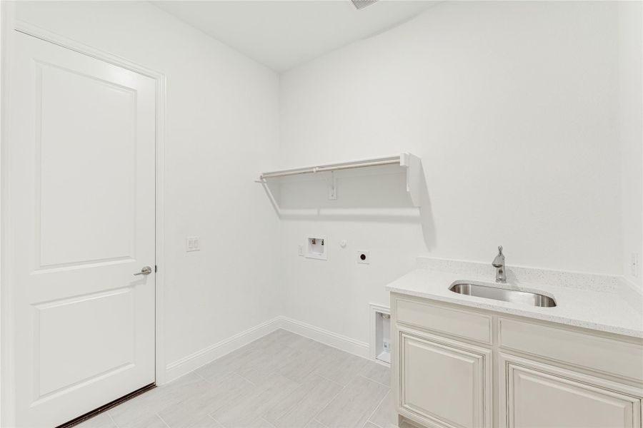 Laundry room with utility sink, white cabinets, wall shelf, and washer and dryer hookups on tile floor