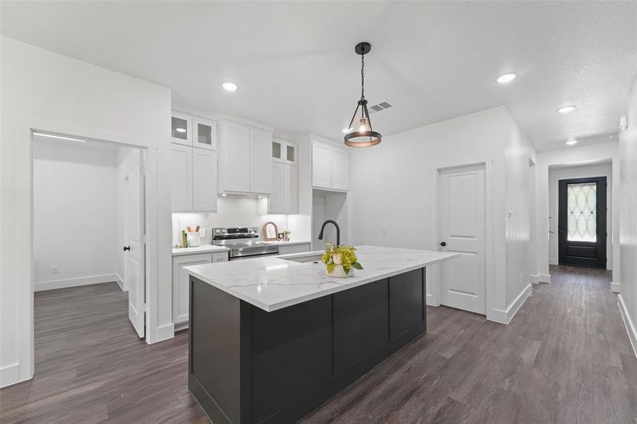 Modern kitchen featuring white shaker cabinetry, stainless steel appliances, a black kitchen island with a white countertop, and wood-finish flooring Modern kitchen featuring white shaker cabinetry, stainless steel appliances, a black kitchen island with a white countertop, and wood-finish flooring