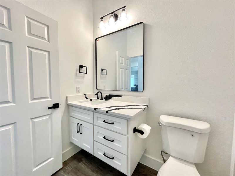 Half bathroom with toilet, vanity, wood finished floors, and baseboards Half bathroom with toilet, vanity, wood finished floors, and baseboards
