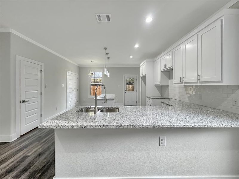 Kitchen with a peninsula, white cabinetry, light stone countertops, tasteful backsplash, and crown molding Kitchen with a peninsula, white cabinetry, light stone countertops, tasteful backsplash, and crown molding