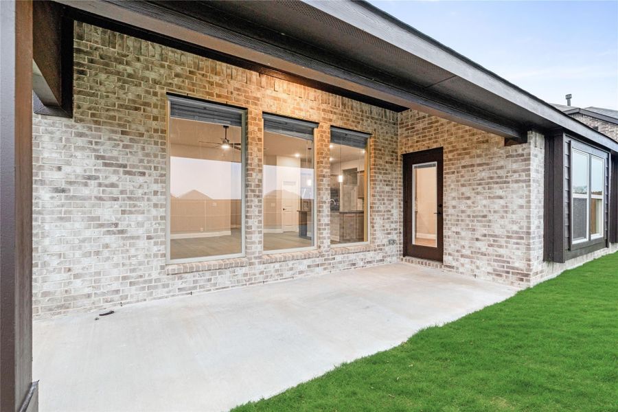 Covered back patio with concrete slab, brick exterior, large windows, and back door overlooking green lawn