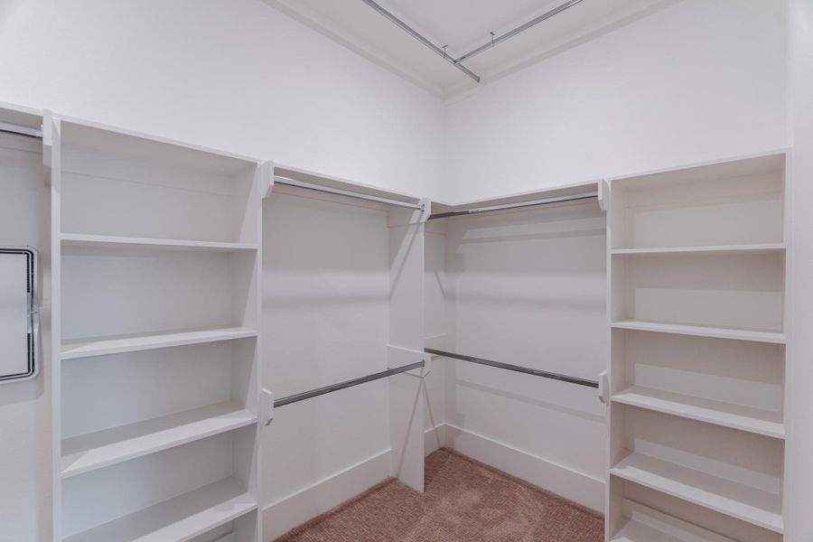 This photo shows a spacious walk-in closet with ample shelving and hanging space, featuring a neutral color scheme and carpeted flooring.Photo Disclaimer: Photos are representative of the community and may depict a similar floor plan, model home, or previously completed residence. This photo shows a spacious walk-in closet with ample shelving and hanging space, featuring a neutral color scheme and carpeted flooring.Photo Disclaimer: Photos are representative of the community and may depict a similar floor plan, model home, or previously completed residence.