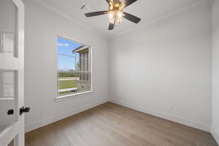 Room featuring wood-finish flooring, a ceiling fan with integrated lighting, a multi-pane window, and crown molding
