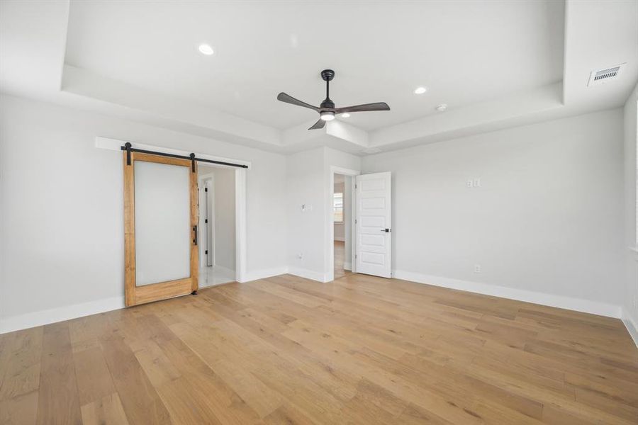 Unfurnished bedroom with light wood-type flooring, a raised ceiling, ceiling fan, and a barn door