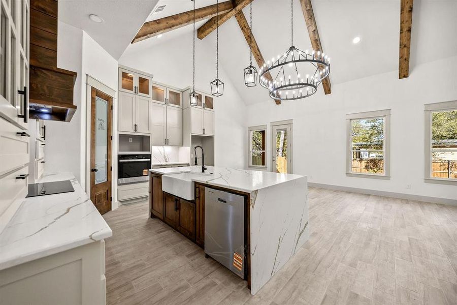 Kitchen featuring high vaulted ceiling, glass insert cabinets, light stone counters, a kitchen island with sink, and appliances with stainless steel finishes