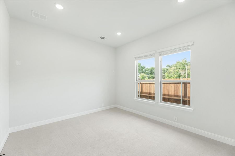 Empty bedroom with white walls, carpet flooring, recessed lighting, and double windows overlooking a wood fence.