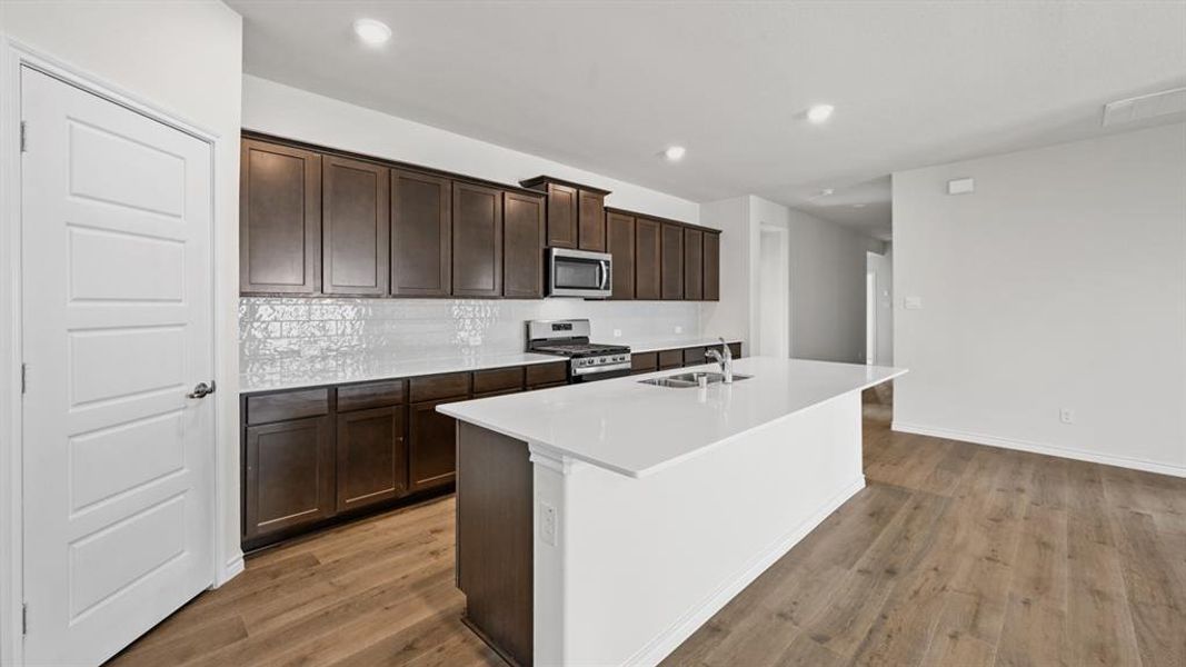 Kitchen featuring dark wood cabinetry, a white tile backsplash, and a large central island with a white countertop and integrated sink