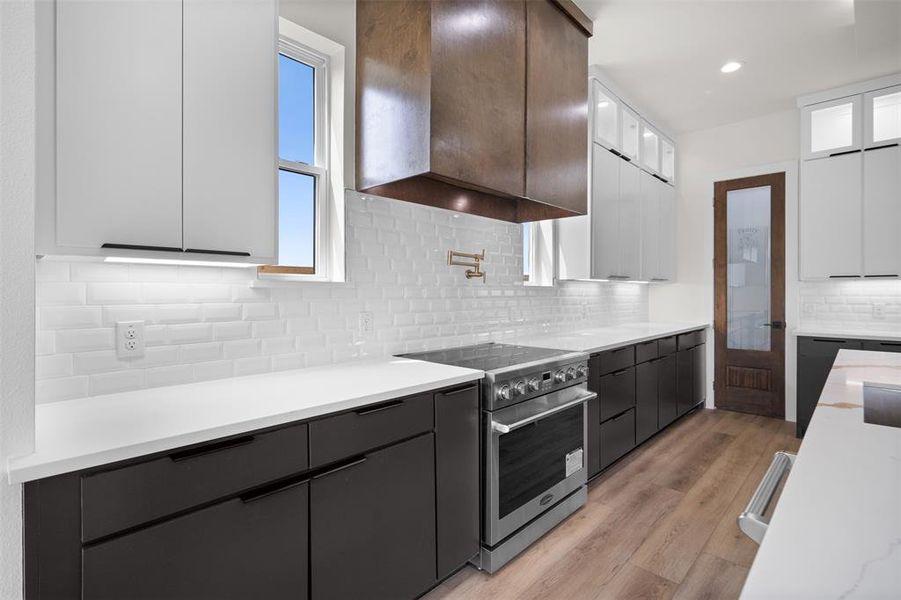 The kitchen features sleek dark base cabinetry with white countertops, complemented by white subway tile backsplash, and light-colored flooring The kitchen features sleek dark base cabinetry with white countertops, complemented by white subway tile backsplash, and light-colored flooring