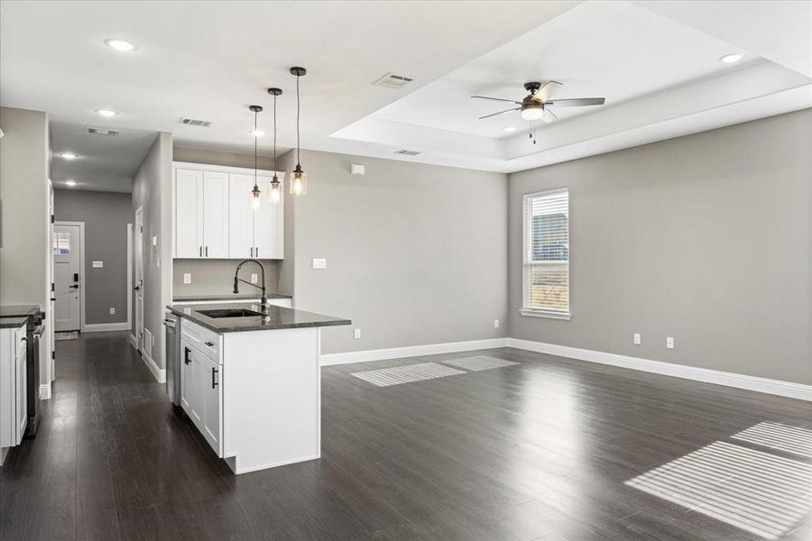 Kitchen featuring sink, hanging light fixtures, a tray ceiling, an island with sink, and white cabinets