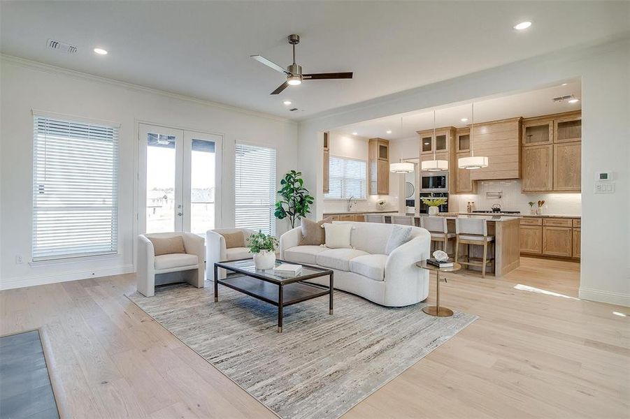 Living room with ceiling fan, light wood-type flooring, crown molding, and french doors to covered back patio with fireplace