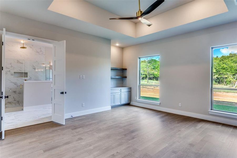 Unfurnished bedroom with a raised ceiling, a ceiling fan, connected bathroom, and light wood-type flooring Unfurnished bedroom with a raised ceiling, a ceiling fan, connected bathroom, and light wood-type flooring