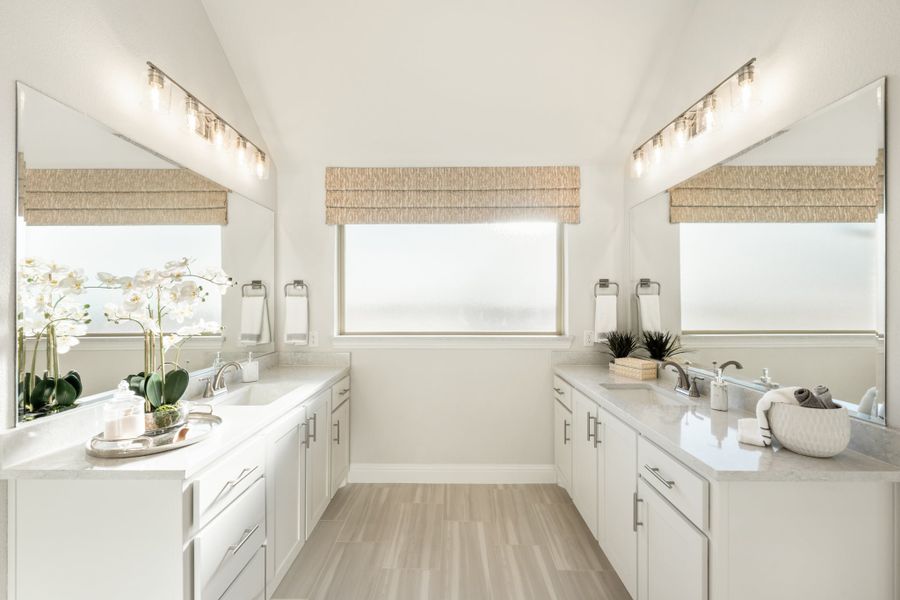 Dual-vanity master bathroom with white cabinets, quartz countertops, large mirrors, and light wood floors